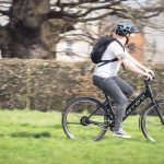 A student riding their Carrera Actuate Lowstep Hybrid bike to university through a park